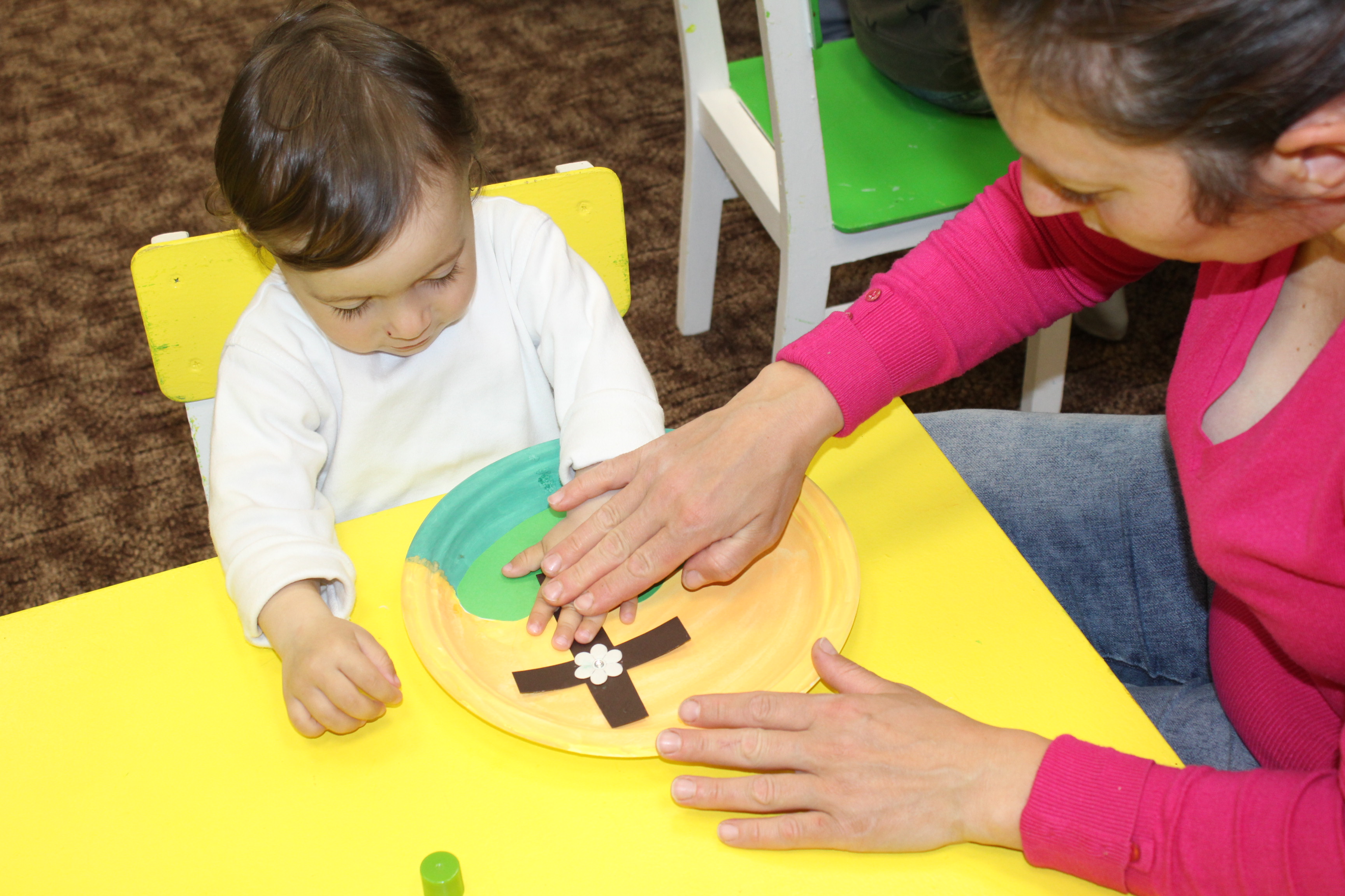 An infant child with an adult, practicing arts and crafts. 