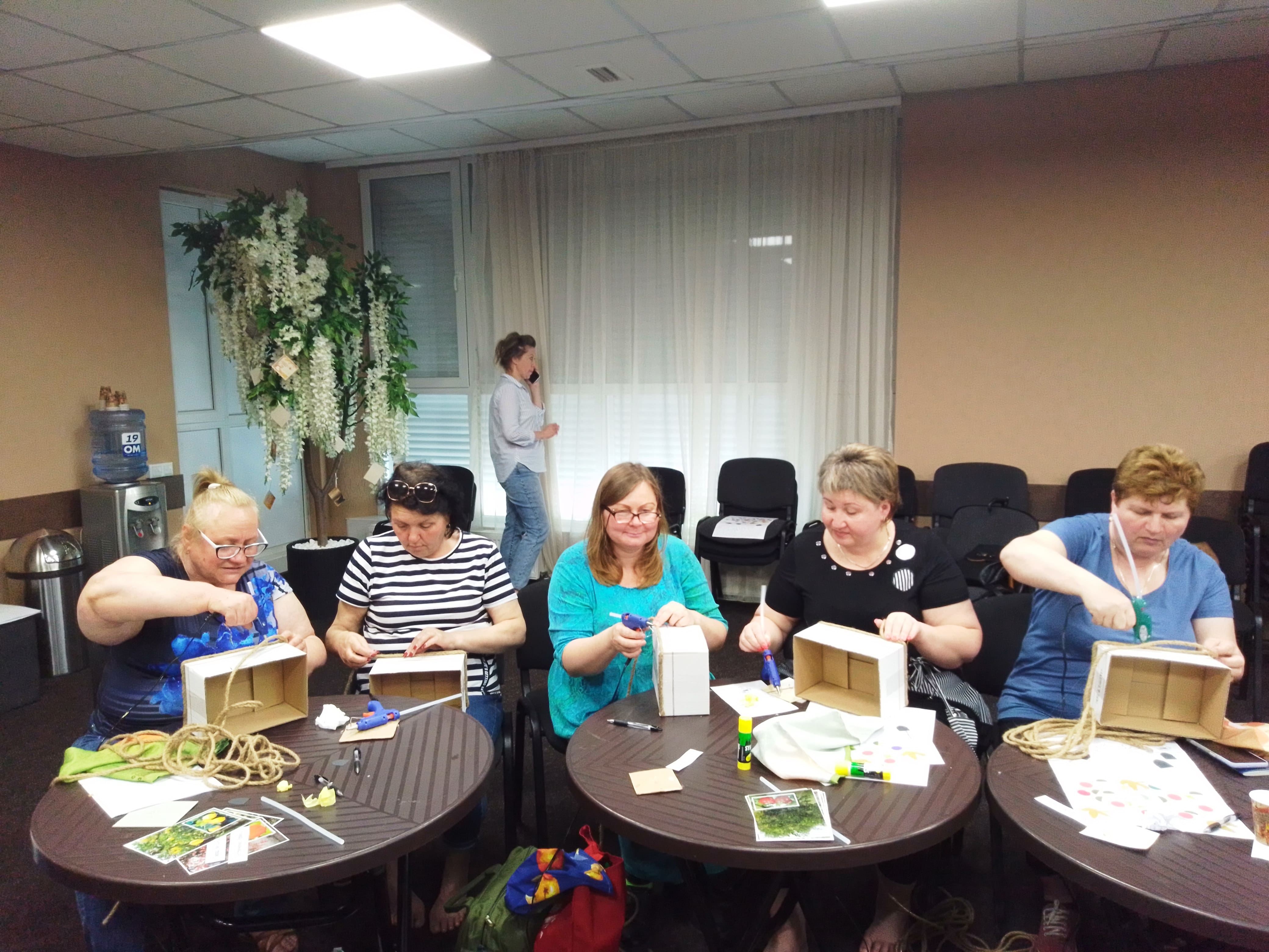 a group of older women practicing arts and crafts around a table. 