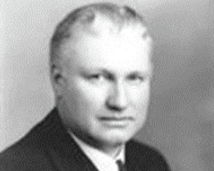 A black and white portrait of a middle-aged man with short hair, wearing a suit and tie.