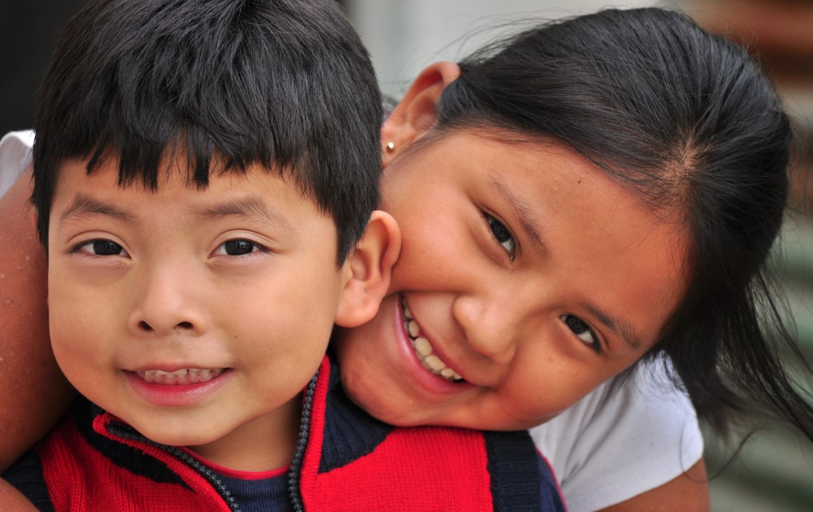 Two smiling children, a boy and a girl, happily embracing each other.