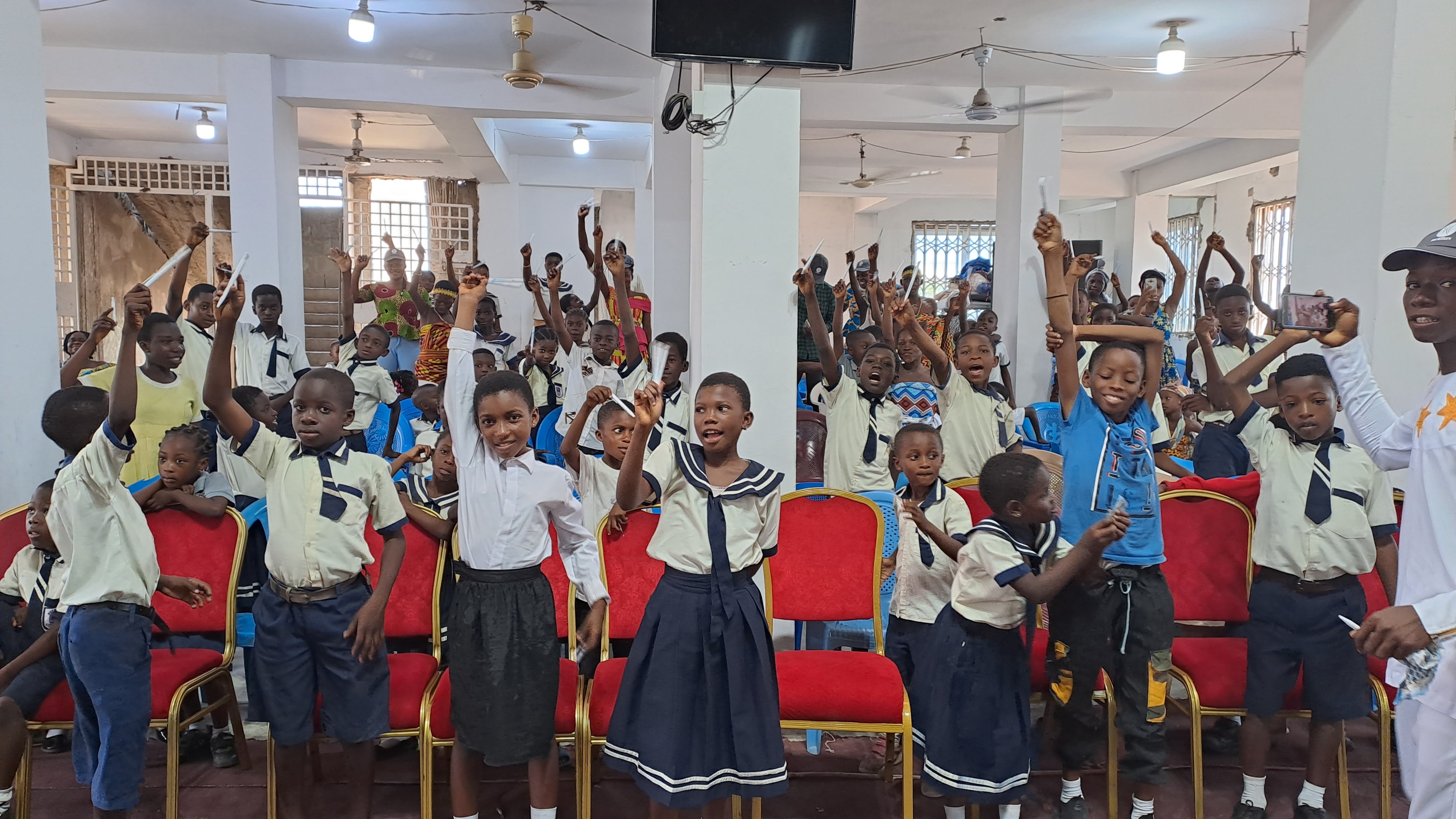 A large group of children raising their hands whilst attending a church ceremony. 