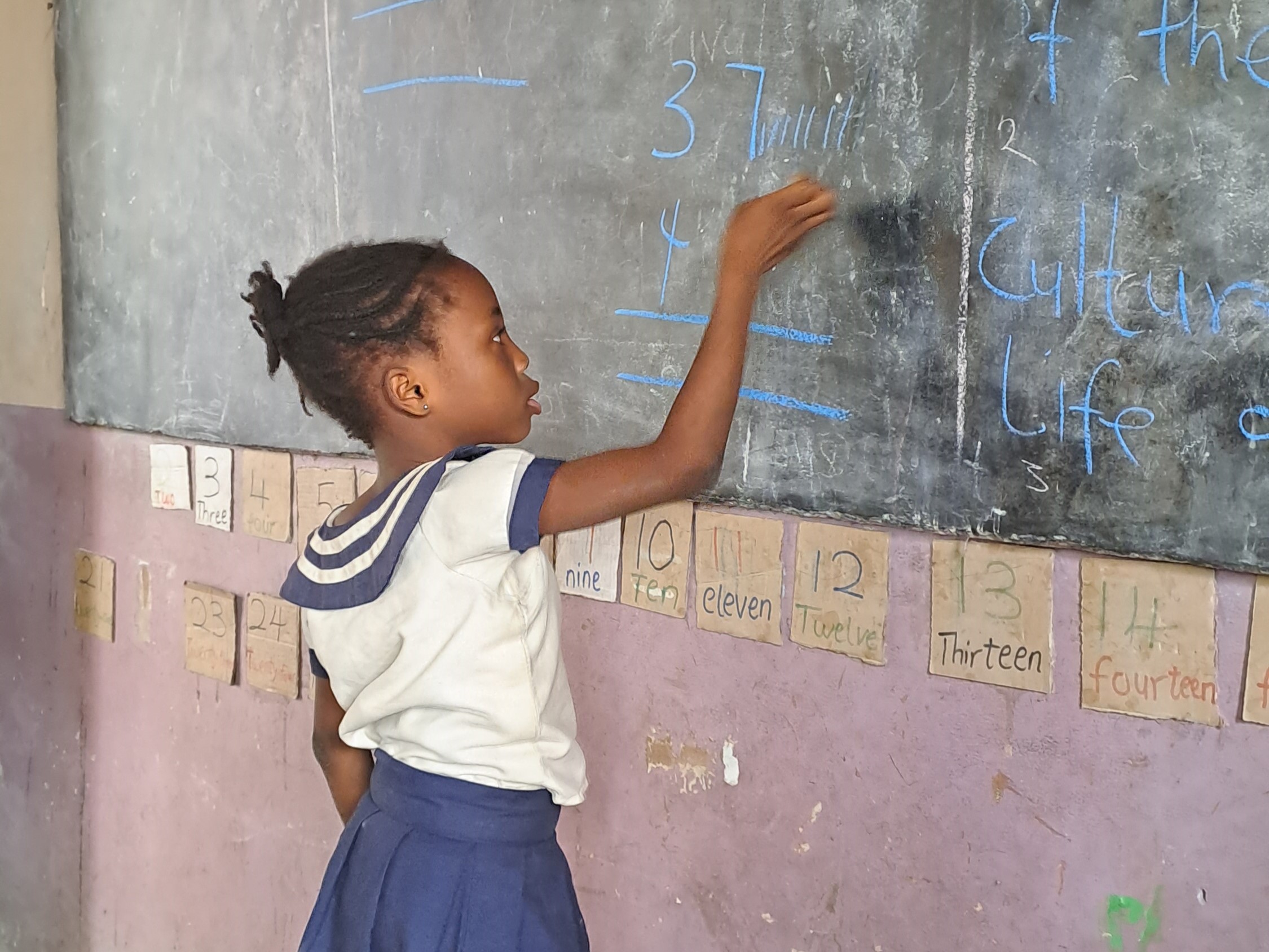 A young girl writing on a chalk board at school 