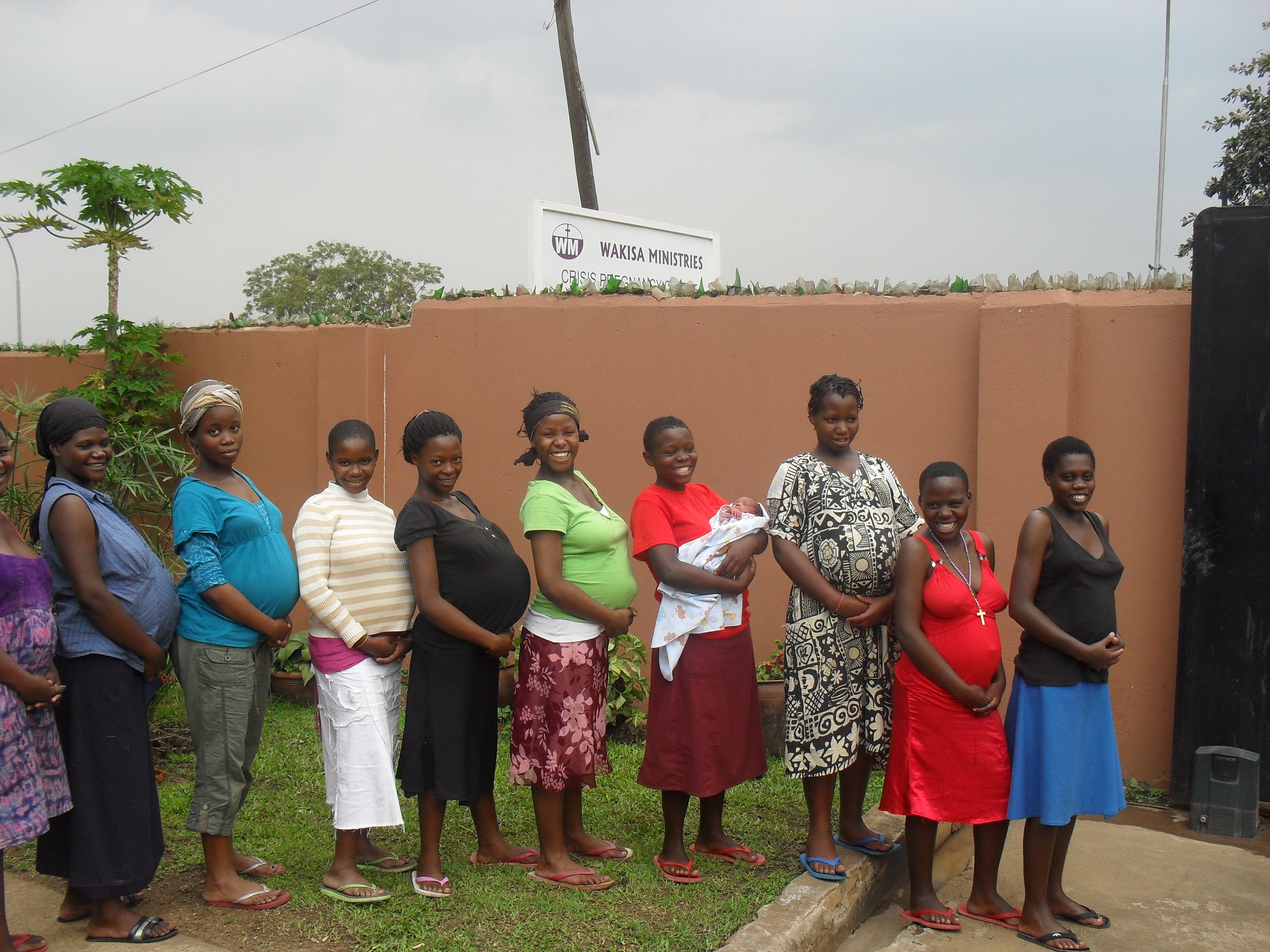 a group of nine pregnant ladies lined up in a line, smiling at the camera 