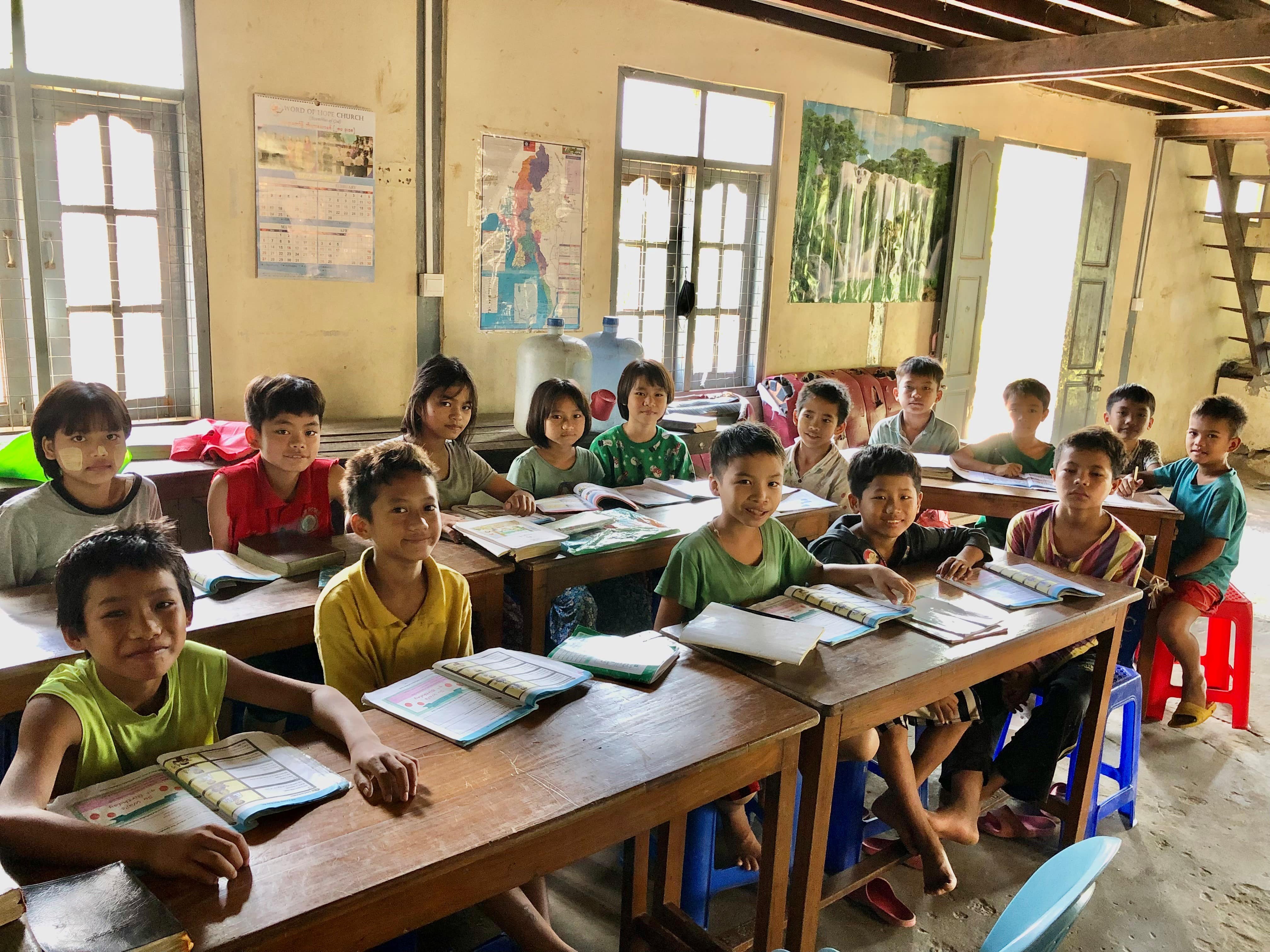 a group of young school children smiling at the camera during a lesson. 