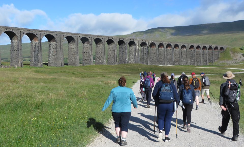 A group of hikers walking outdoors, a bridge and mountains off in the distance. 