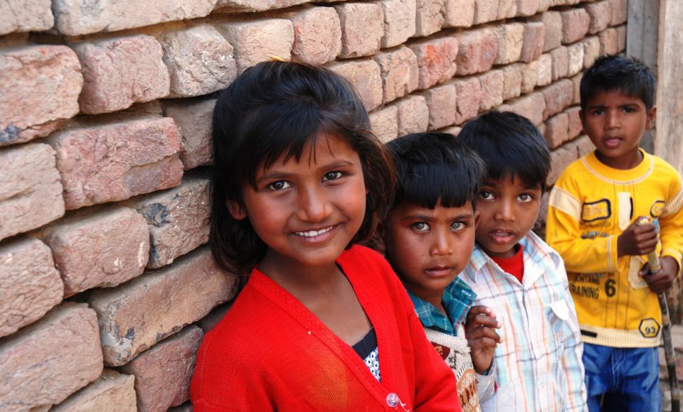 Four young children are standing against a brick wall, smiling and looking at the camera.