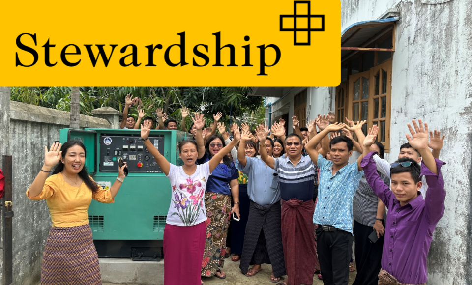 A large group of men and women raising their hands whilst smiling for the camera. 