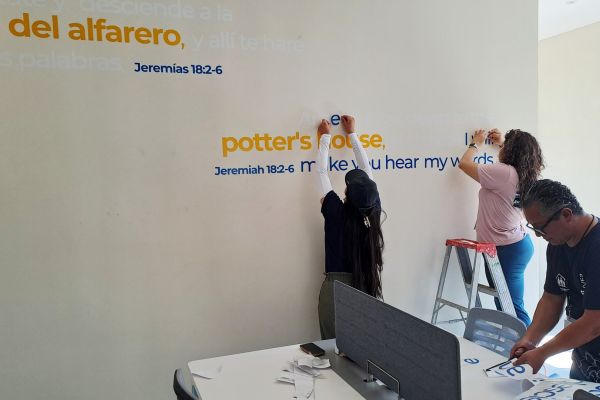 Potter’s House team applying bilingual Bible verse lettering to an indoor wall