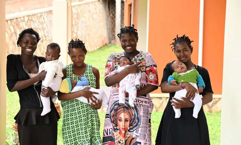 A small group of people sitting outside on sane outside of a hut, listening to someone reading from the Bible