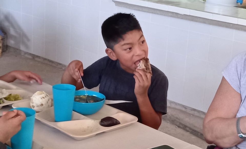 A young boy eating his lunch, smiling for the camera.