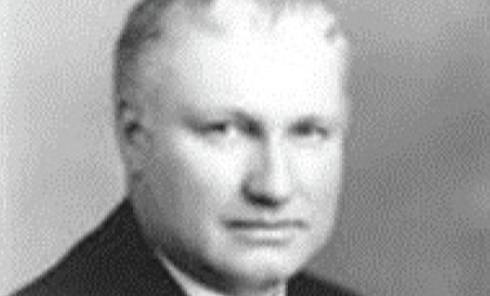 A black and white portrait of a middle-aged man with short hair, wearing a suit and tie.