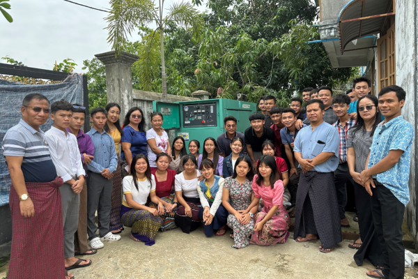 a large group of people gathered outside, looking towards the camera for a photo.