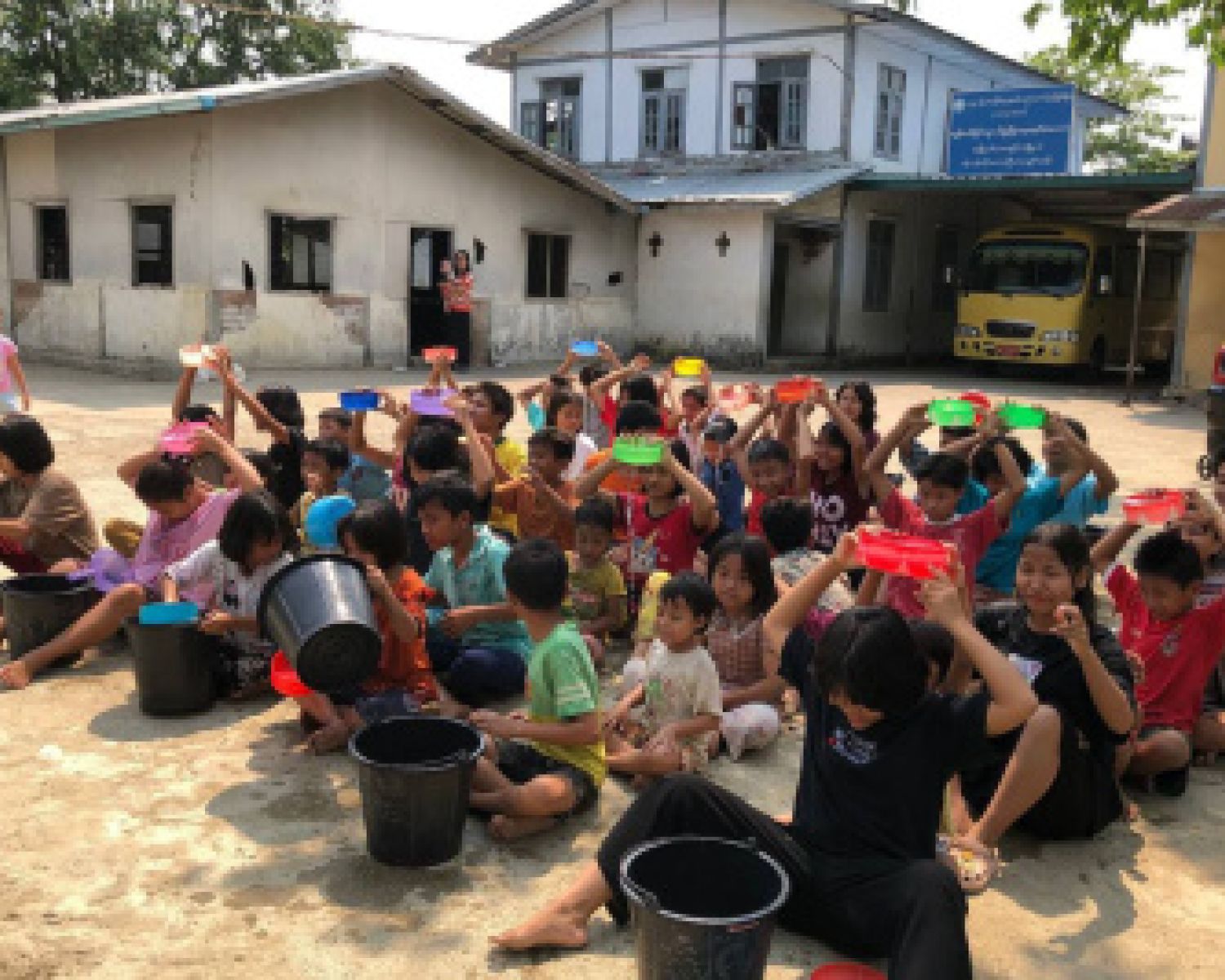 A classroom of children sitting outside in the sun. 