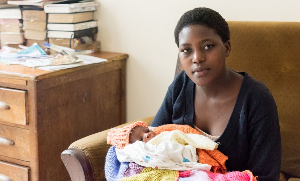 a young mother looking into the camera whilst holding her newborn baby. 