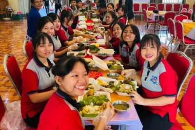 A group of young people smiling for the camera whilst having some dinner around a table.