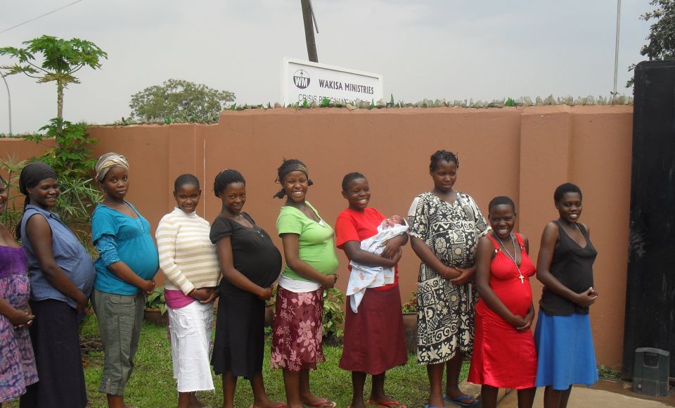 a group of nine pregnant ladies lined up in a line, smiling at the camera 
