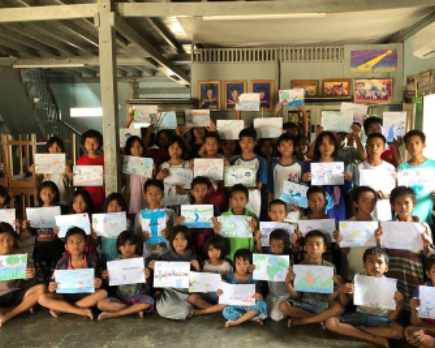 A classroom of children holding up their art to the camera. 