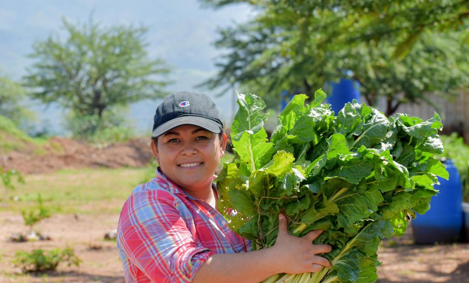 A woman holding crops smiling at the camera 