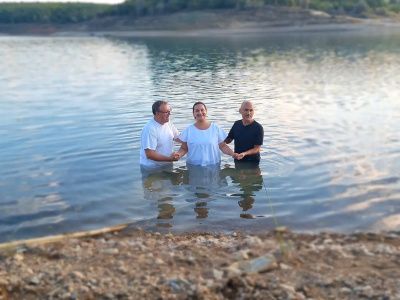 A woman being baptised outside by two men in a lake.